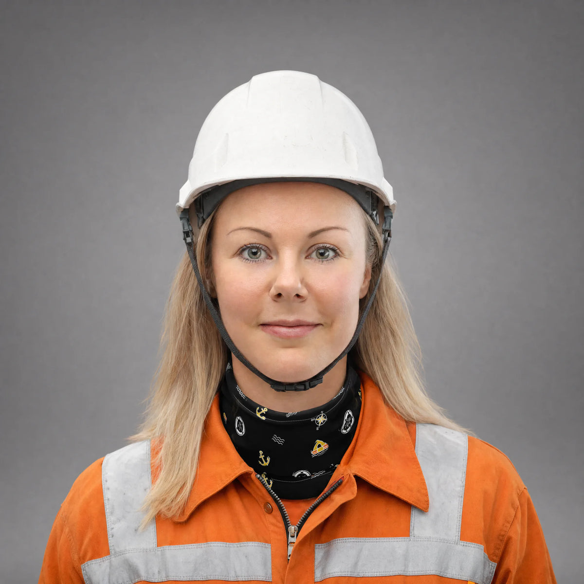 Female seafarer in an orange coverall and white hard hat wearing the Safety at Sea neck gaiter around the neck