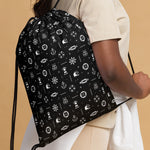 Black drawstring bag with white patterns held by a person against a beige background