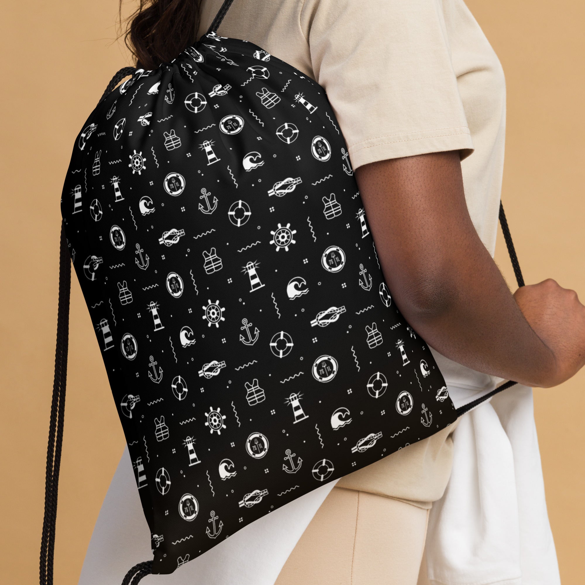 Black drawstring bag with white patterns held by a person against a beige background