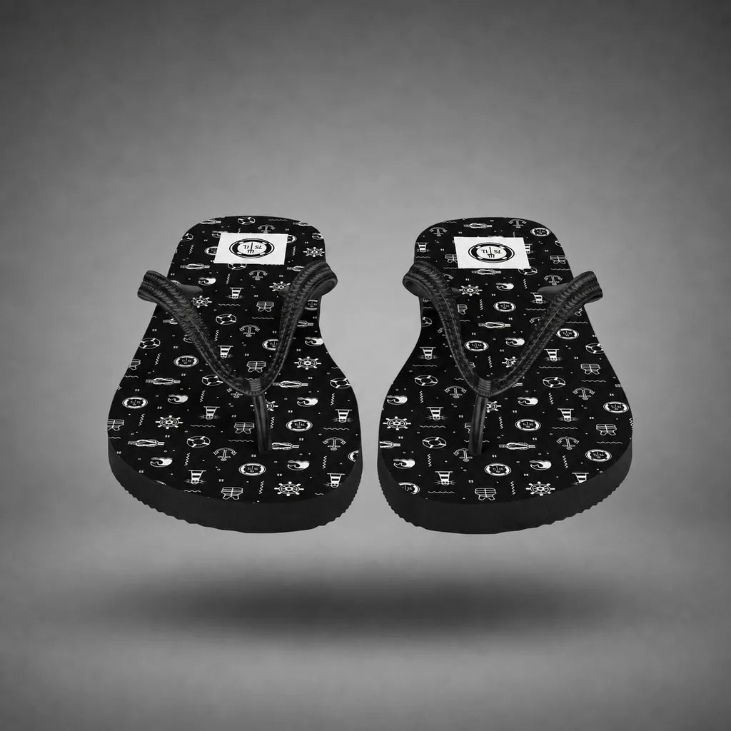Detail view of black Beach Activity flip-flops with nautical icon pattern, floating above a grey studio floor with a soft shadow.