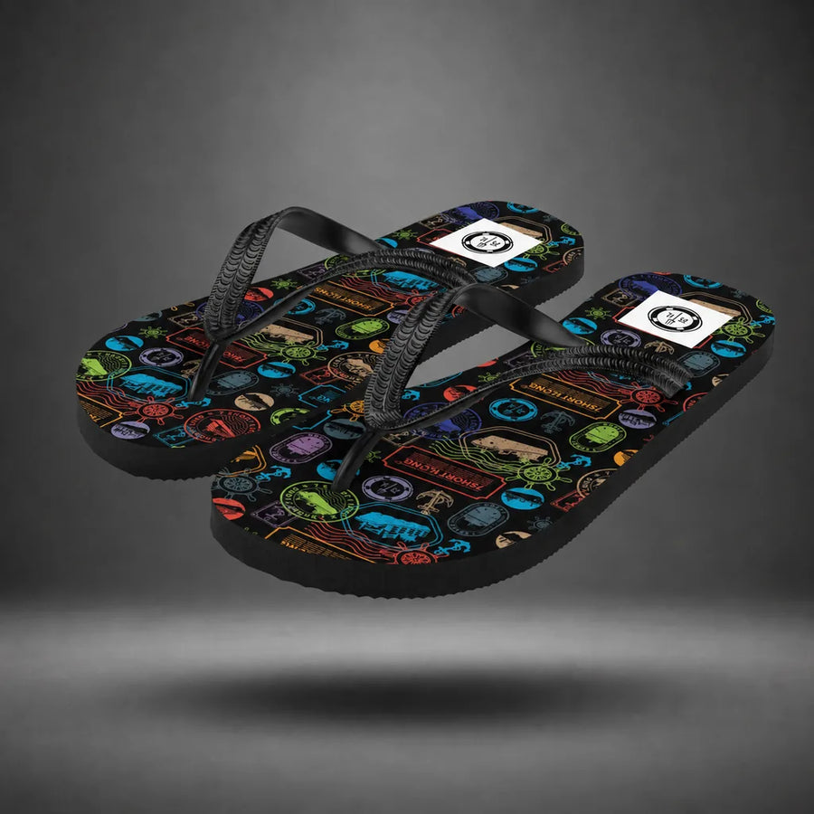 Pair of black World Cruise flip-flops with passport stamp pattern, floating above a grey studio floor with a soft shadow.